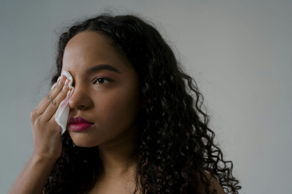 A thoughtful woman with curly hair wipes her eye using a tissue.
