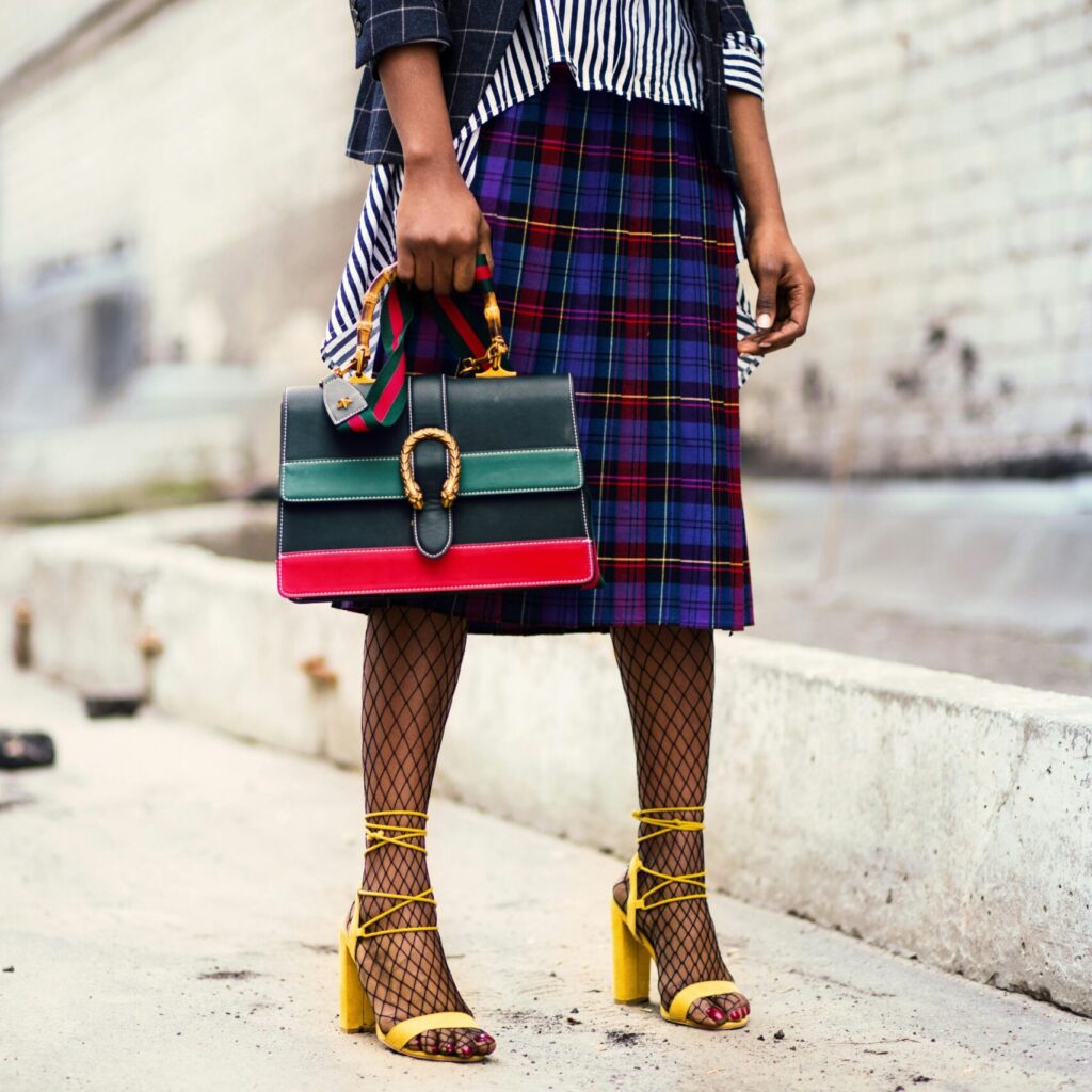 Fashion-forward outfit with plaid skirt and colorful handbag in urban setting.
