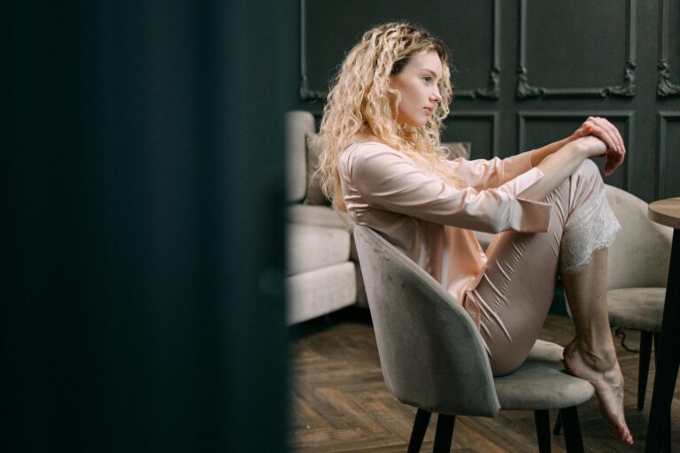 Woman wearing pajamas sitting barefoot on a chair at home, showcasing relaxation.