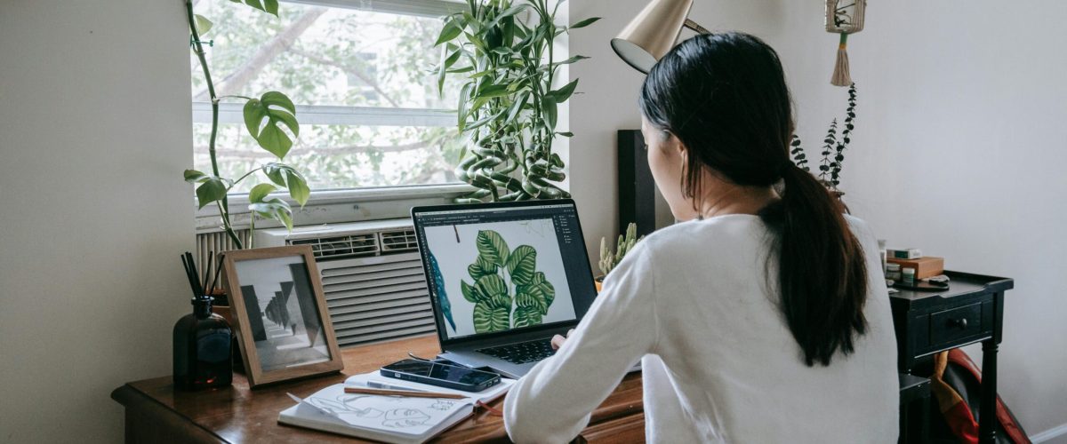 Woman working on a laptop in a plant-filled home office, embodying a modern freelance lifestyle.